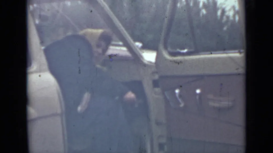 The woman remains beside the open vehicle door, bending toward the seat area in grainy 1967 Saint Petersburg footage.