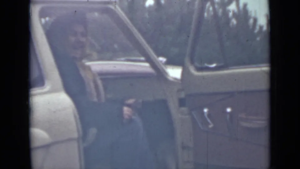 A woman appears partly seated inside the vehicle, with her face faintly visible through soft, scratched 8mm footage from 1967 Saint Petersburg.