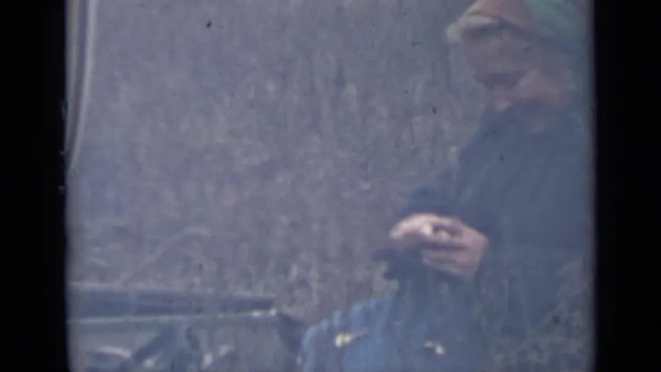A woman in a green dress sits outdoors near the car area, her face partly visible in faded 1967 home-movie footage.