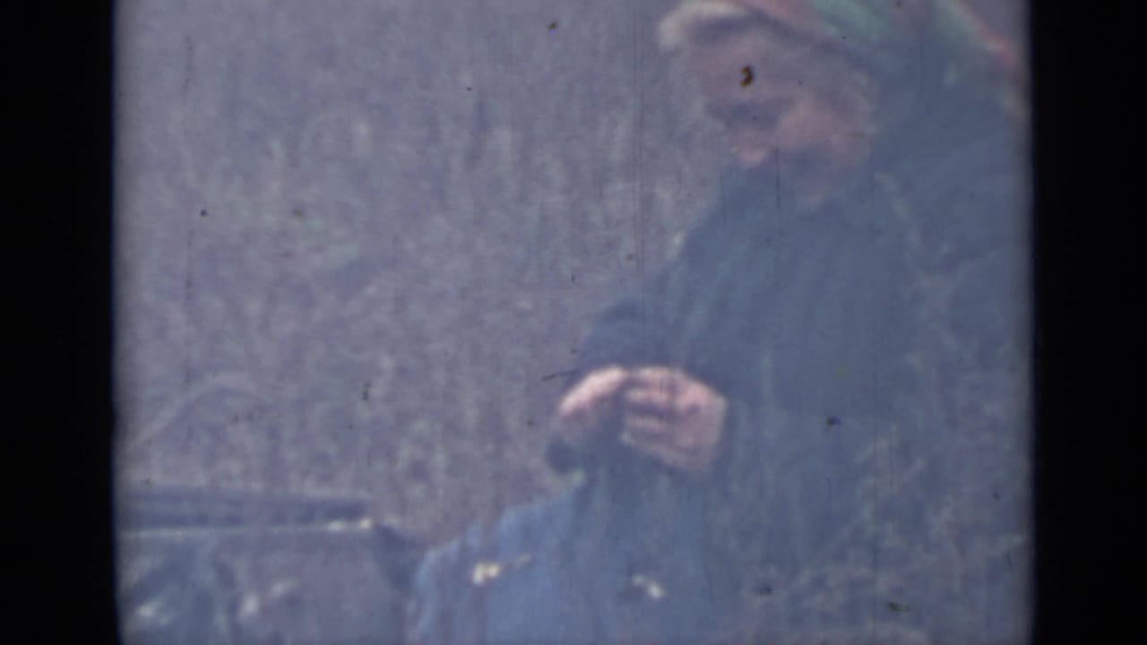 Adult woman in a headscarf and dark coat appears to peel food outdoors, consistent with the supplied 1967 Saint Petersburg home-movie metadata.