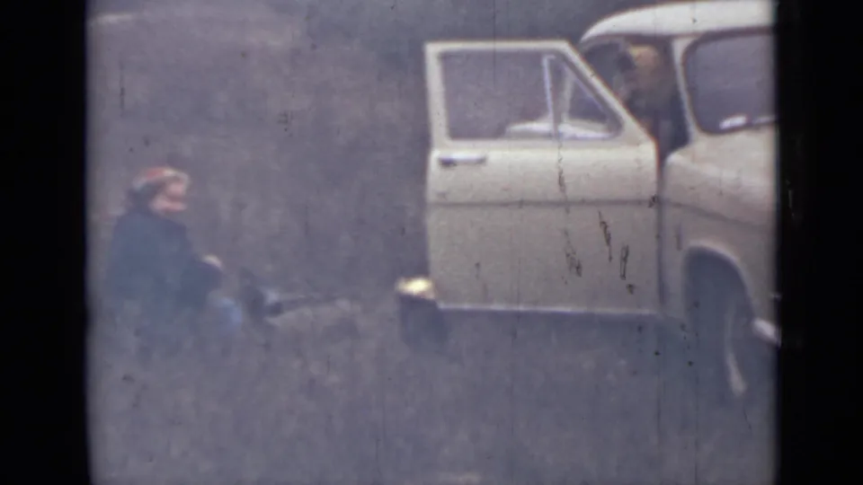 A wider 8mm view shows the woman low to the ground near vegetation, with a white car and open door in the background.