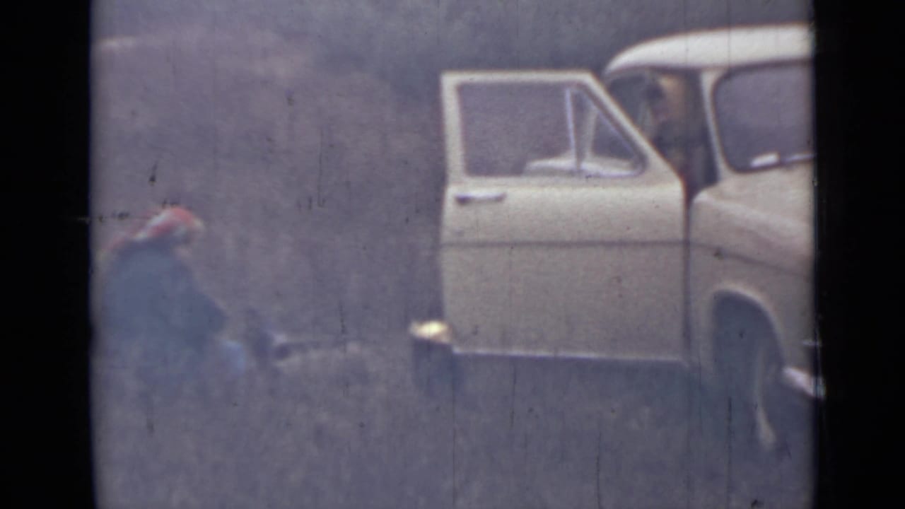 Crouching person in a red hat beside an open white car door.
