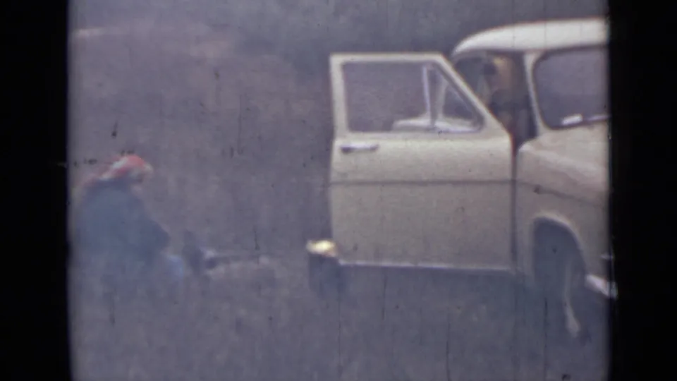 1967 Saint Petersburg home-movie frame showing a crouching person near gear beside an open white vintage car door.