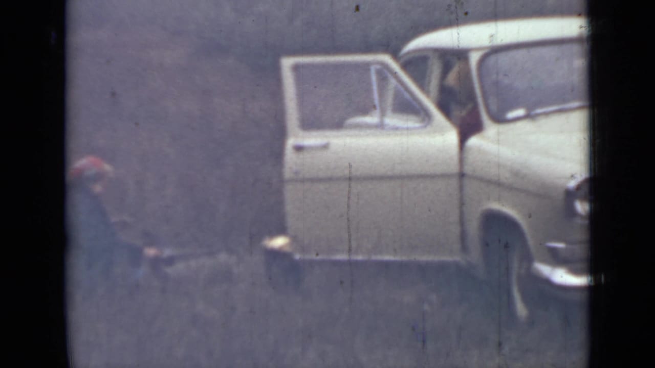 White car with open door and a person crouched near gear outside.