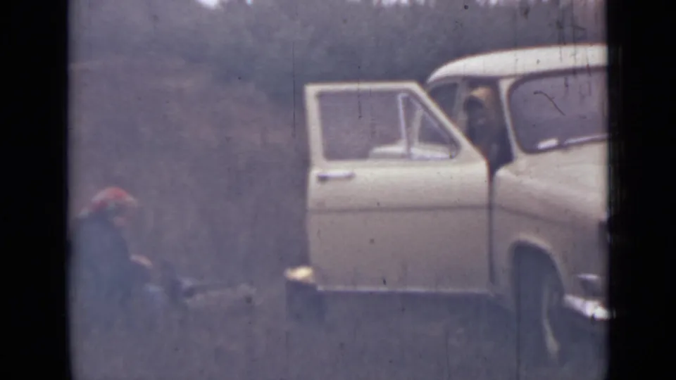 1967 Saint Petersburg 8mm frame showing the front of a white car, open door, seated passenger, and crouching person nearby.
