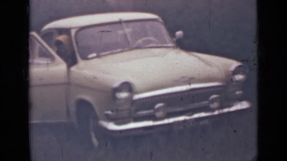 1967 8mm frame near Saint Petersburg showing a light-colored older sedan parked among trees with a door open.