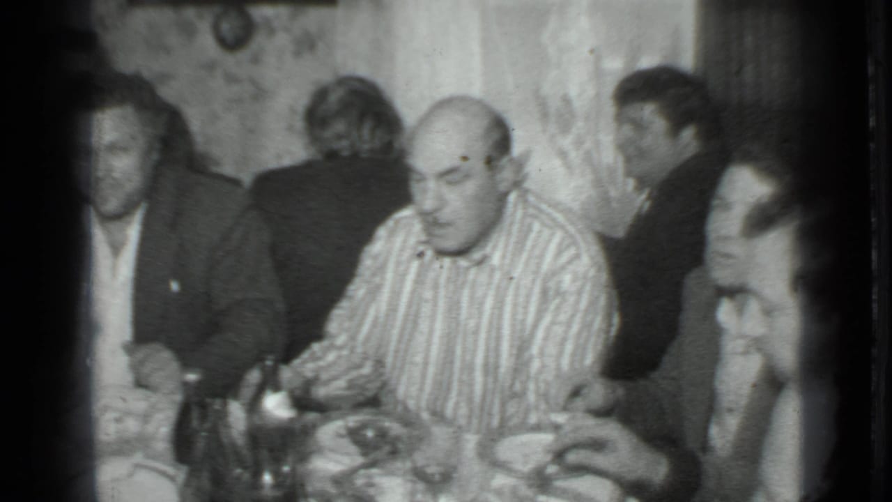 Men sit closely at a table while one man in a striped shirt faces downward.