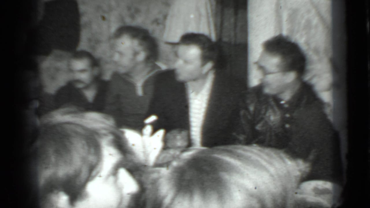 Adults seated closely around a dinner table in a dim home interior.