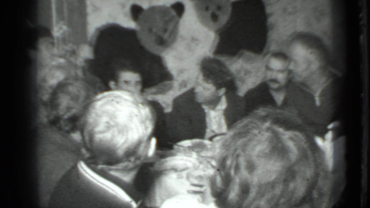 Group of adults gathered at a table with a large bear decoration behind them.
