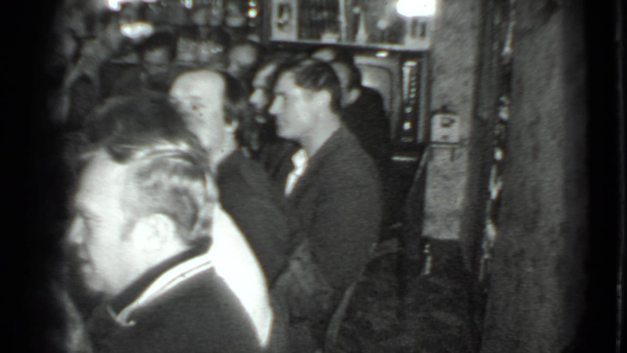 Adults seated and standing near a table with shelves and a television behind them.