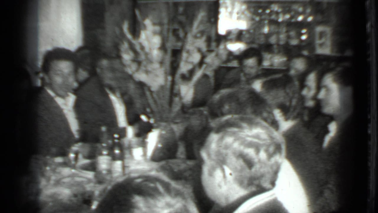 1975 Moscow dinner gathering with adults around a table, visible bottles, wall decor, and soft 8mm exposure.