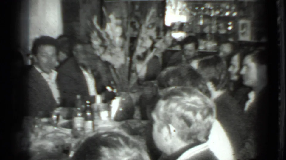 1975 Moscow dinner gathering with adults around a table, visible bottles, wall decor, and soft 8mm exposure.