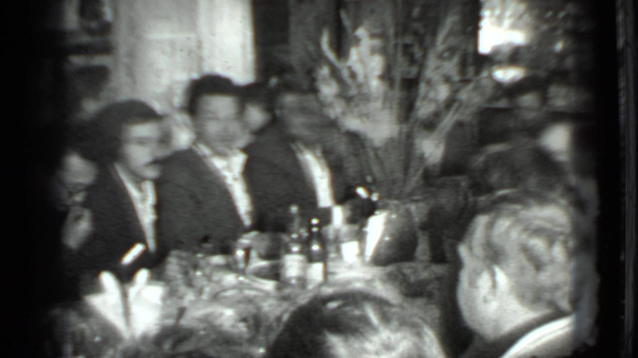 Black-and-white 8mm frame from the Moscow 1975 clip showing adults in suits seated at a dinner table during a private gathering.