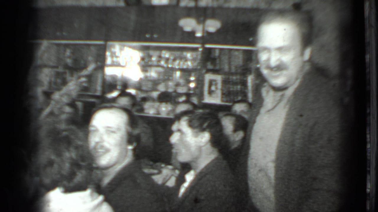 Moscow 1975 home-movie frame showing a smiling man standing by a seated group during an indoor dinner gathering.