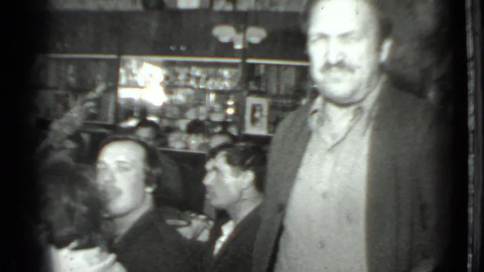 1975 Moscow home-movie frame showing adults gathered in a dim bar or restaurant interior with bottles and glassware visible.