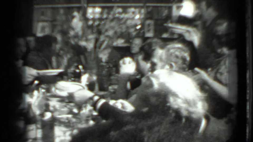 Black-and-white 8mm view of a full dining table in Moscow, with adults sharing food amid bottles, plates, and wall decorations.