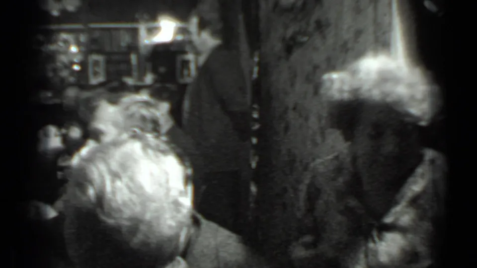 Soft 8mm frame from a Moscow dinner gathering showing diners in the foreground and a waitress standing in the restaurant interior.
