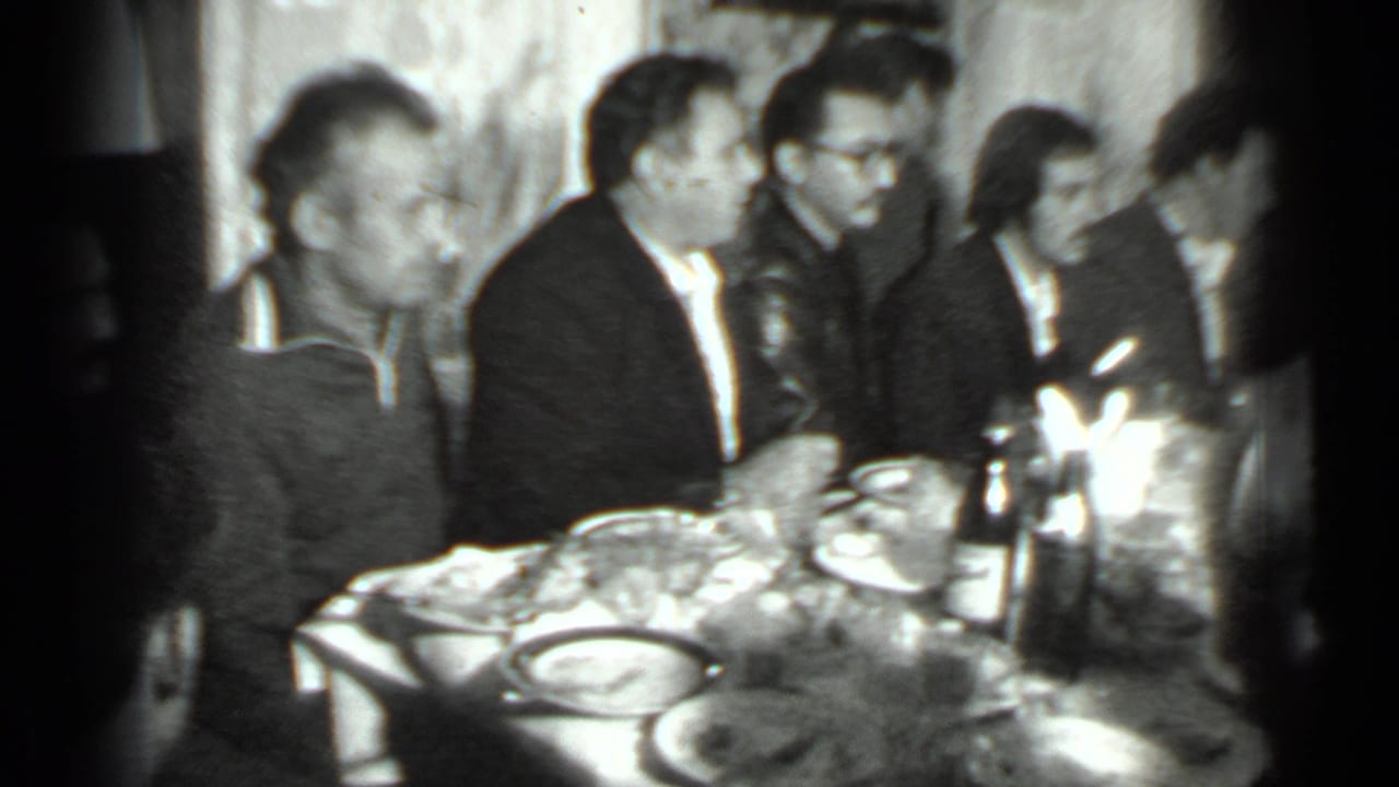 Adults seated around a crowded dining table with plates, bottles, and glasses.