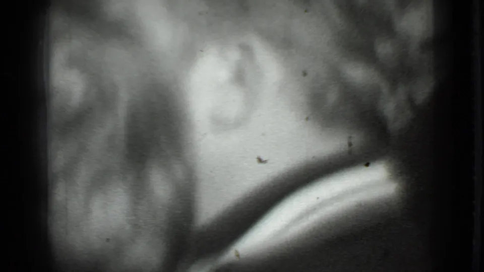 Black-and-white 8mm frame from the Moscow clip with a soft profile, visible ear, hair, and dark surrounding tones.