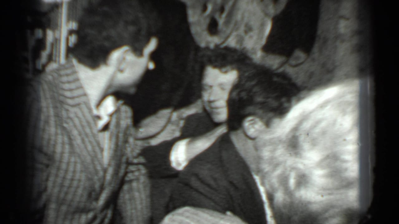 A man in a striped shirt leans over a seated man while others crowd around in a dim room.