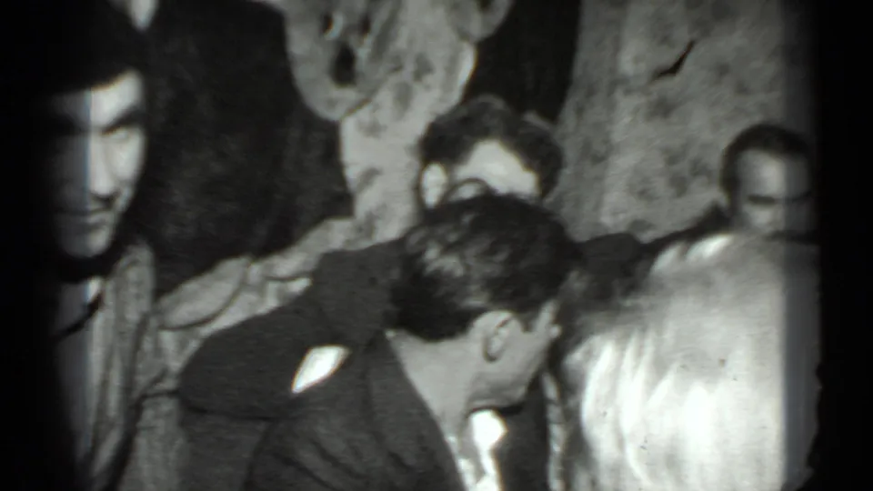 The 1975 Moscow home-movie frame shows several adults in a crowded private interior, partially blocked by nearby heads.