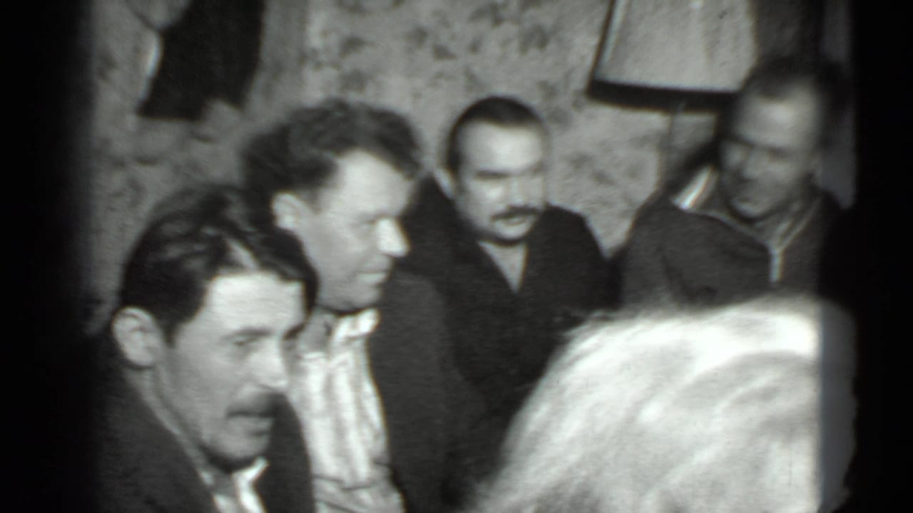 Four adult men gathered indoors, with several faces visible in soft black-and-white film.