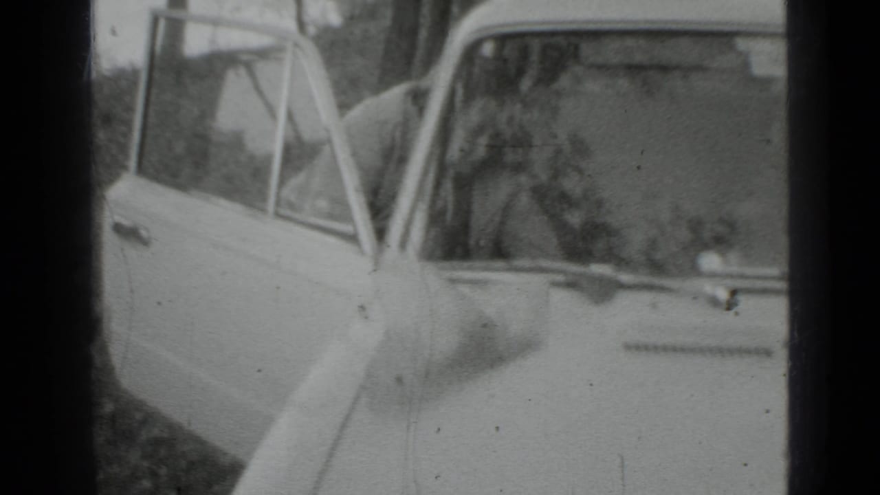 Vintage car seen closer with the open door and a person partly obscured behind it.