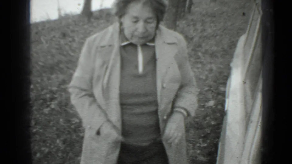 The woman moves away from the car in a 1975 Moscow outdoor home-movie shot, with trees and ground cover behind her.