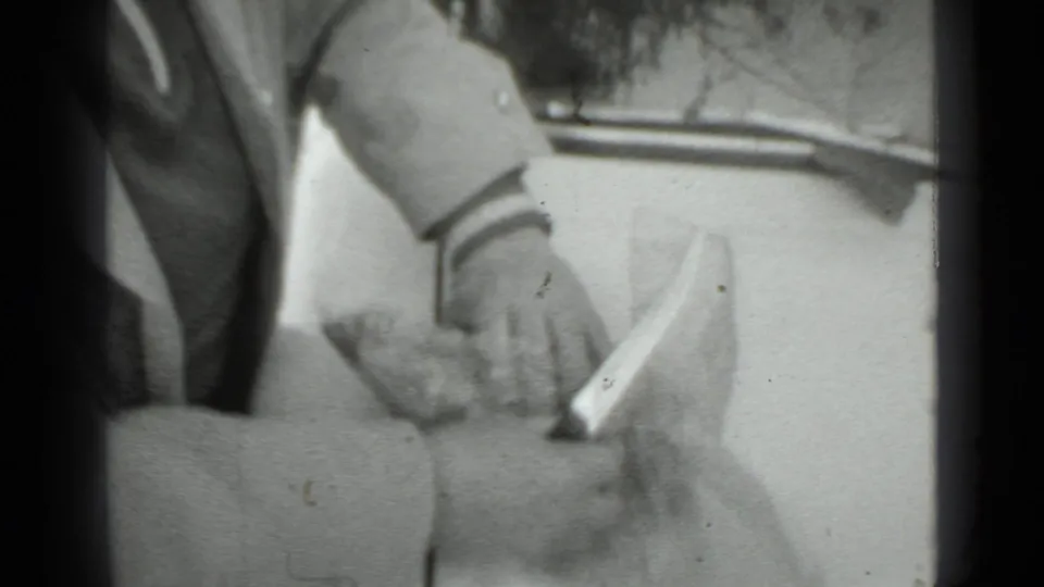 The woman handles a small wrapped or food-like item on the car hood during the 1975 Moscow home-movie moment.