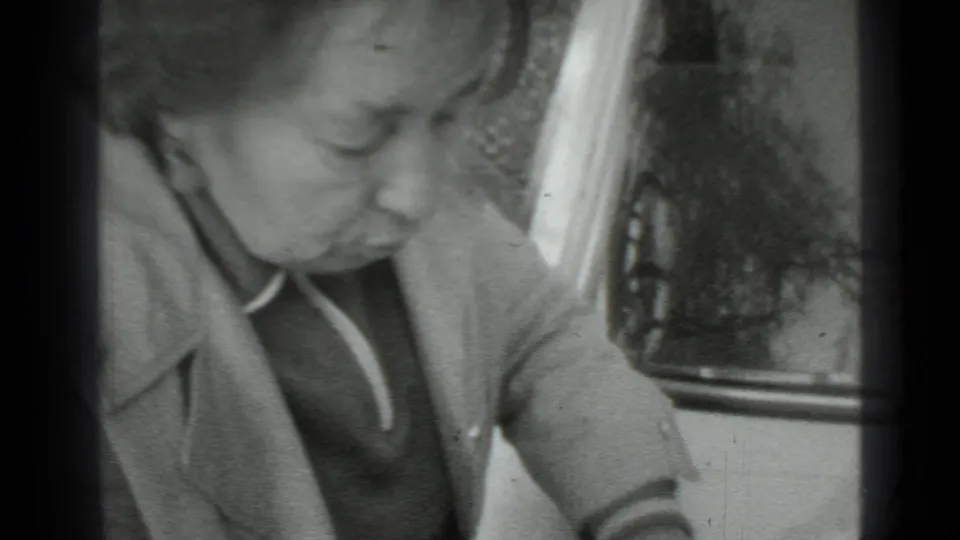 The woman remains bent beside the car door and hood, focused on something just below the frame in 1975 Moscow footage.