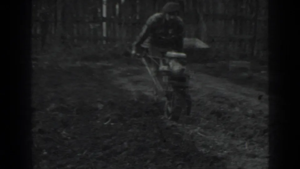 In Moscow 1975 8mm footage, a man in dark clothing guides a small hand-pushed tiller through a garden plot.
