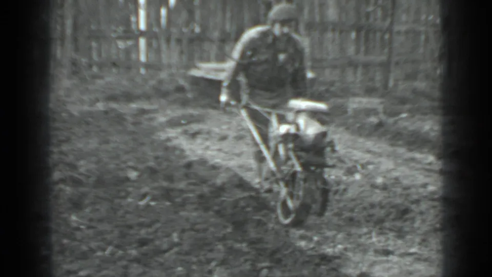 A man in dark outerwear moves away from the camera with a small tiller in a Moscow garden plot.