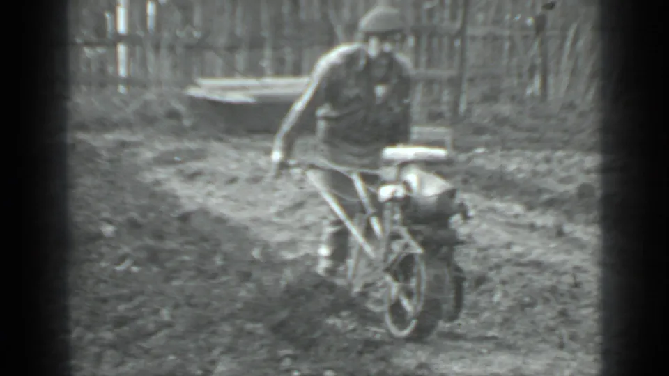 The 1975 Moscow home-movie frame shows a man steering a compact tiller toward the camera in a garden.