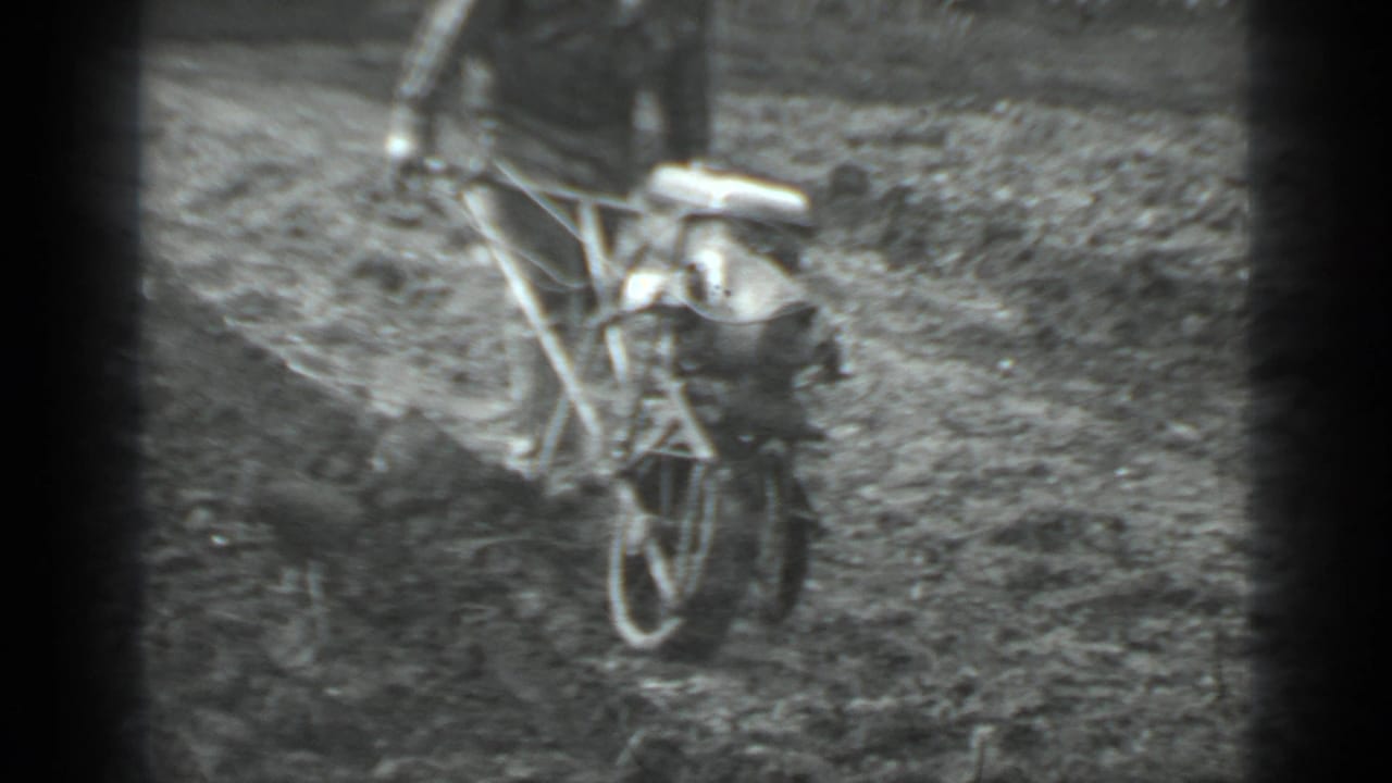 Man guiding a small walk-behind plow across loose soil in a field.
