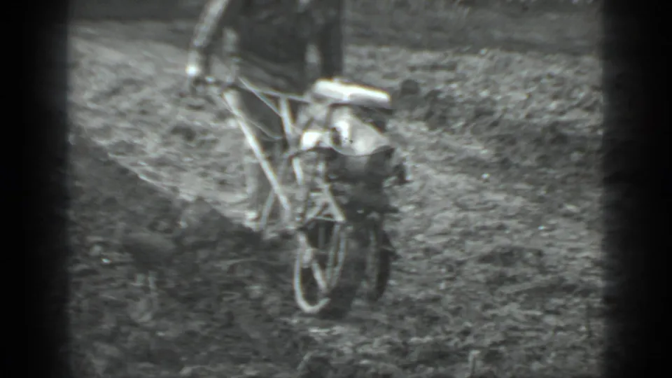 1975 Moscow-area home-movie frame showing a man in dark clothing operating a small walk-behind plow in a rough field.
