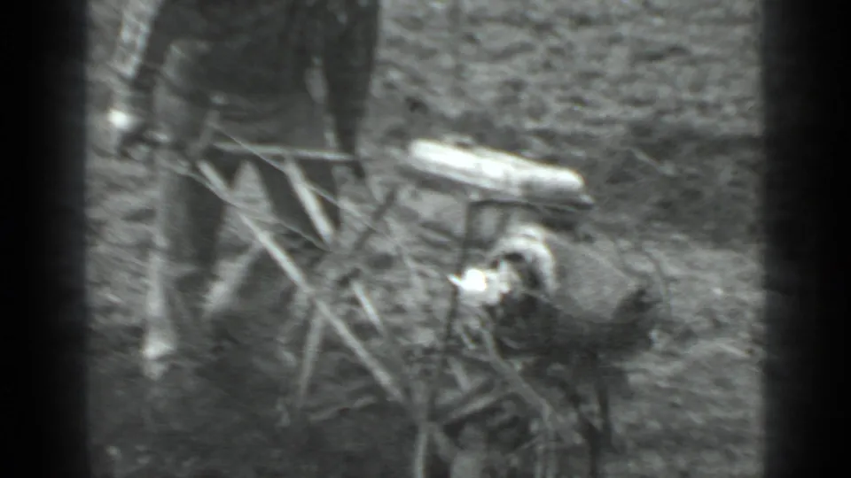 Grainy 8mm frame showing the operator beside the walk-behind plow, with the machine body and soil in close view.