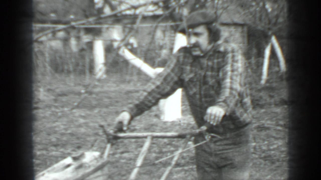 Man in a cap and plaid shirt holding the handle of a push mower.