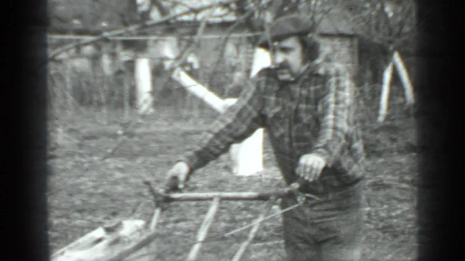 A man in a cap and plaid shirt stands with a push mower in an outdoor Moscow yard, supported by the clip metadata.
