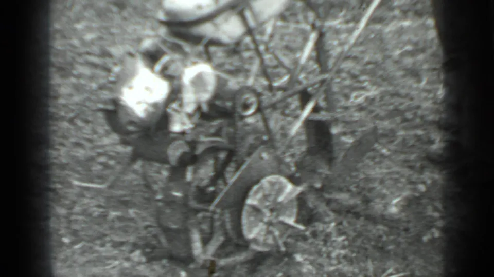 1975 Moscow-area home-movie frame of a man near a small wheeled grass cutter among grass and brush.