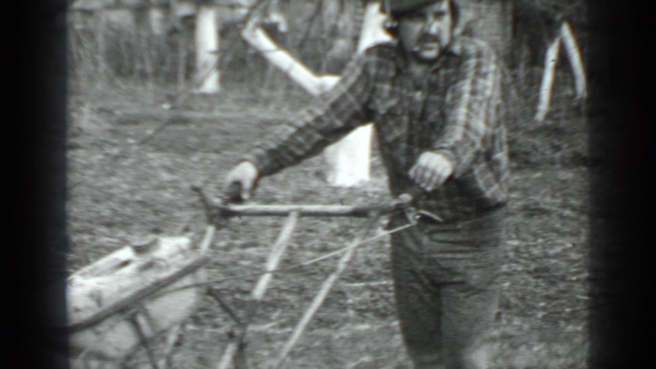 Man in plaid shirt holds the handle of a small cutting machine outdoors.