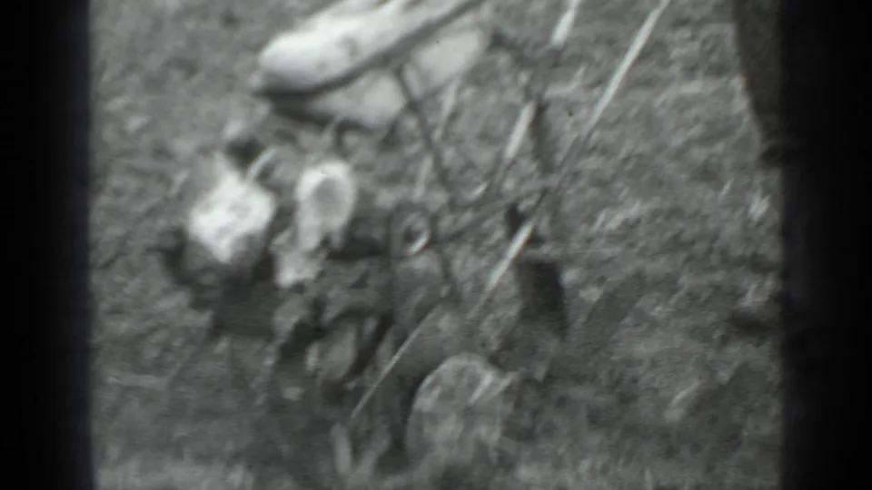 Soft-focus 8mm frame showing the man and wheeled grass cutter from above in the rural setting.