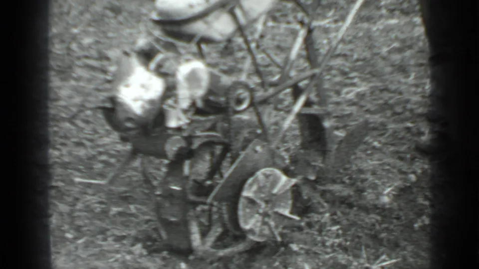 Close overhead 8mm view of the vintage grass cutter and operator in a 1975 Moscow rural scene.