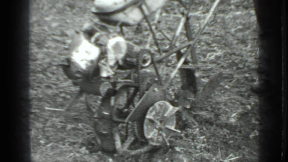 In supplied 1975 Moscow home-movie footage, a man bends beside a small tiller amid soil, grass, and yard debris.