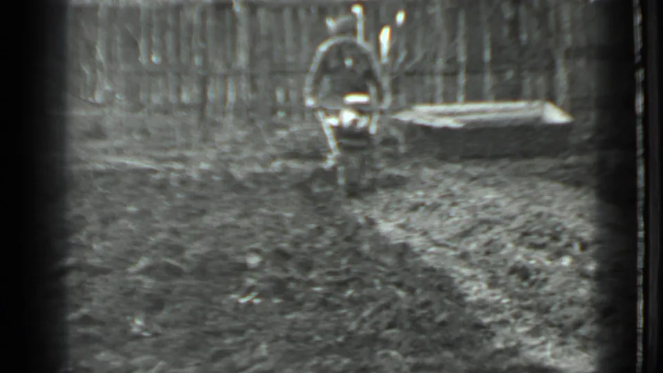 A man operates a small motorized tiller in a fenced garden yard, consistent with the supplied 1975 Moscow metadata.