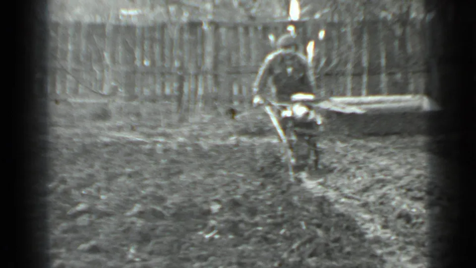 The handheld 8mm frame shows the man moving the tiller through loose soil in a fenced Moscow garden yard.
