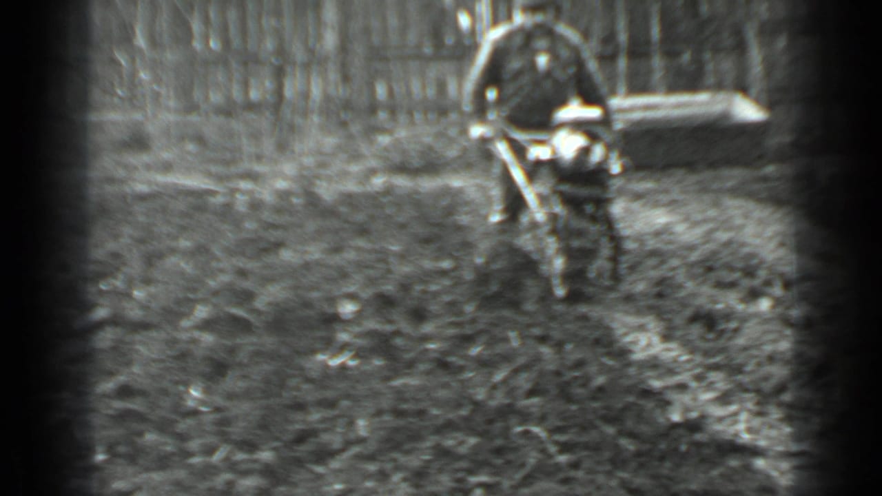 Man continues guiding the small cutter through mud with a fence behind him.