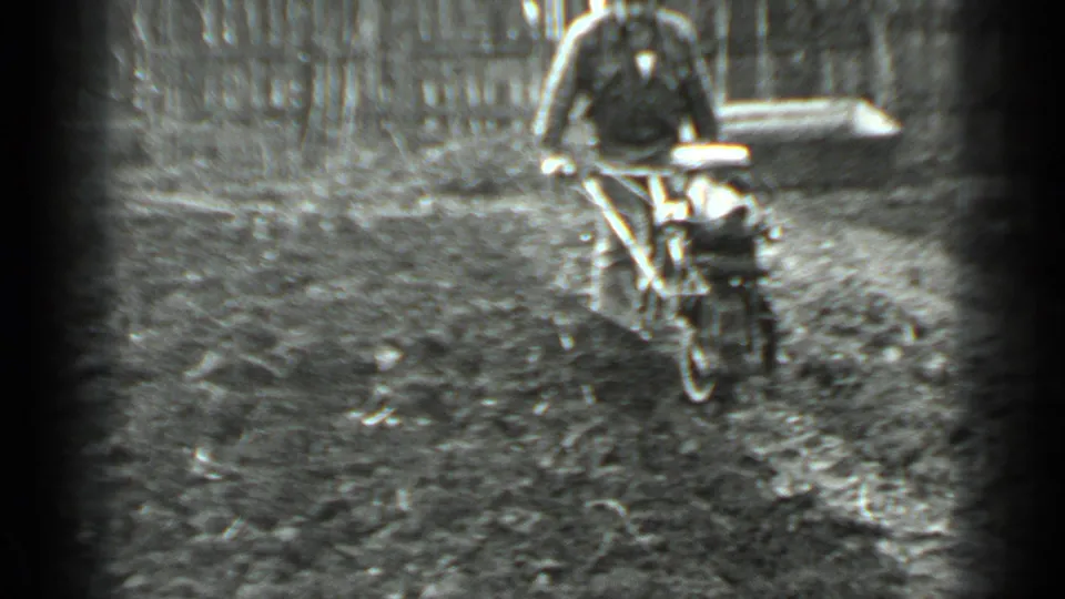 In the grainy 8mm frame, the man grips the machine handles while working across the muddy fenced area near Moscow.