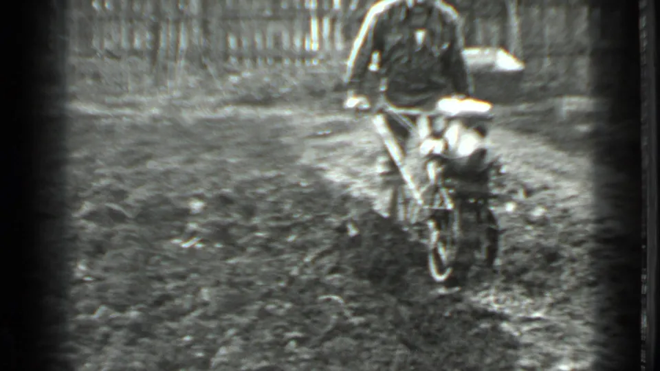 The man and small cutter move nearer the camera, with soft 8mm focus and a wooden fence still visible behind them.
