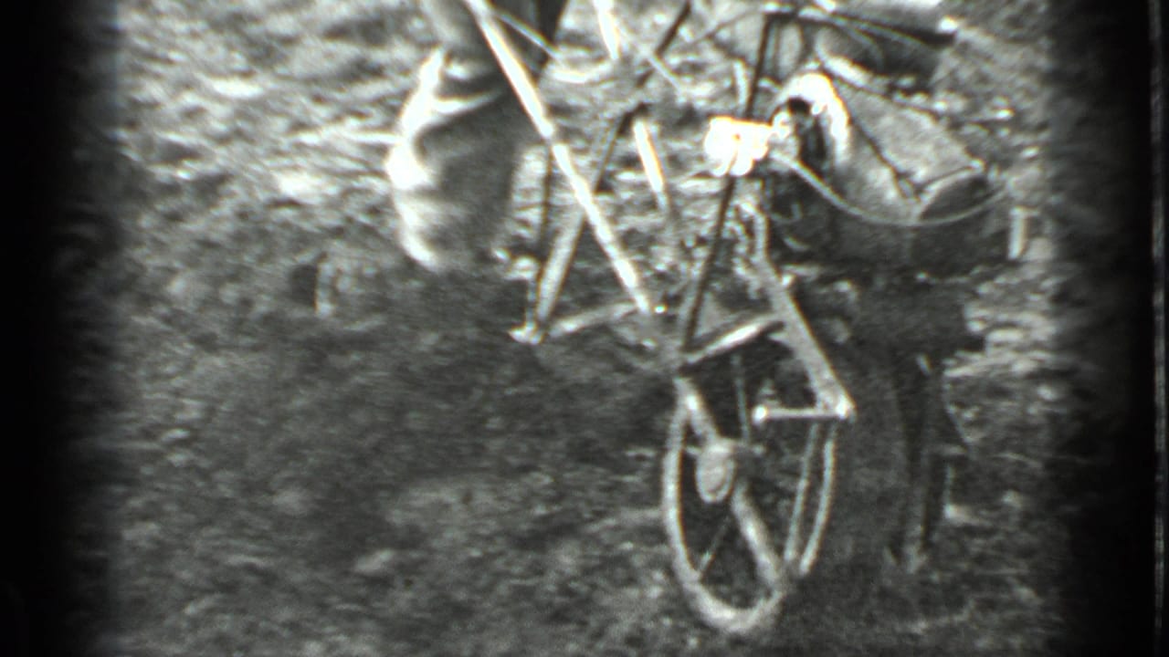 Man guiding a small hand tiller through rough soil near garden foliage.