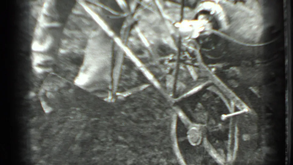 A rear view shows the man pushing the hand tiller across dirt, with branches and soft black-and-white 8mm grain around the frame.